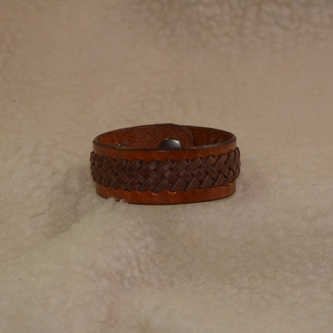 Brown leather 6-3/4 inch long 1 inch wide band bracelet with dark brown 1/2 inch wide center braided applique and metal snap closure. Closed view.