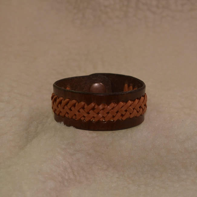 Dark brown leather 6-3/4 inch long 1 inch wide band bracelet with light brown 1/2 inch wide center braided applique and metal snap closure. Closed view.