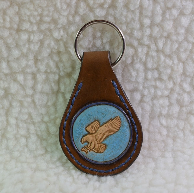 Brown leather tear drop shaped keyfob with a carved eagle surrounded by a raised navy blue circular frame