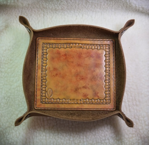 Top view of brown leather tray for keys, change, and other trinkets or as a dice tray, measures about 6-1/2 by 7 by 1-1/2 inches deep and has a decorative panel with a starburst border design and smooth center area