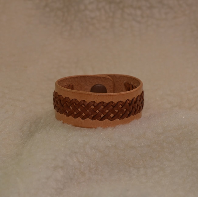 Natural leather 6-3/4 inch long 1 inch wide band bracelet with brown 1/2 inch wide center braided applique and metal snap closure. Closed view.