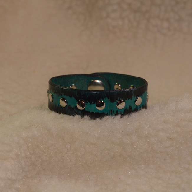 Turquoise and black leather 7 inch long 3/4 inch wide band bracelet with center metal rivet design and metal snap closure. Closed view.